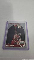Trading card showing Michael Jordan performing a slam dunk in Chicago Bulls uniform, card in protective sleeve with purple edges.