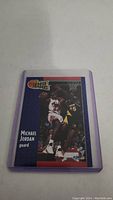 Photo of Michael Jordan basketball card by Fleer showing game action, encased in clear protective sleeve with purple edges.