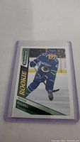 Front of Quinn Hughes rookie hockey card in protective sleeve showing player skating in Vancouver Canucks uniform.
