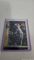 Front view of a Tiger Woods rookie trading card in a purple protective sleeve showing Tiger Woods in mid golf swing with 'Tiger's Tales' and Upper Deck logo.