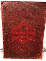 Photo of the front cover of the souvenir book featuring red textured leather-like material embossed with decorative patterns and gold lettering.