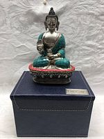 Front and side view of the Buddha sitting statue showing turquoise stone inlays on garments and red stone accents on the base, placed on blue box.
