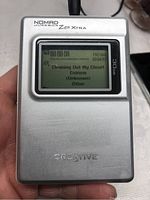 Front view of Creative Nomad Jukebox Zen Xtra 30GB player powered on showing track details on LCD screen including song title, artist, and playback time.
