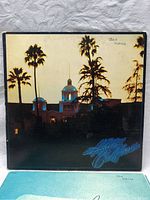 Photo of the front album cover showing building with palm trees in sunset light and 'Hotel California' neon title with handwriting 'Ian Slater'