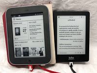 Image of Nook and Kobo e-readers next to each other on a white surface, both powered on showing different screens.