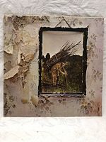 Front of the album cover showing the man carrying sticks and worn floral wallpaper background with peeling and damage.