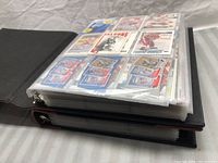 Two full black binders shown stacked, with visible pages of hockey cards in plastic sleeves.