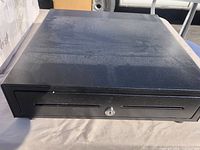 Black metal cash drawer with front key lock, viewed from front and above