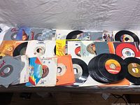 Overview of multiple 45 RPM vinyl records in various sleeves and labels spread out on a surface.