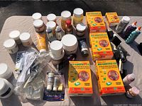 Tabletop view of assorted art supplies including epoxy kits, paint jars and bottles, brushes and adhesives displayed on cloth surface