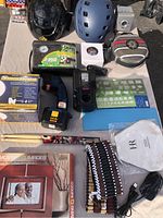 Photo showing various items including two helmets, power drill, charger, photo frame, drumsticks, and decorative beaded item laid out on a surface.