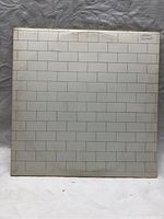 Front cover of the first album showing classic white brick wall design with slight discoloration and signs of wear