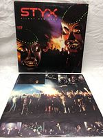 Front cover of Styx Kilroy Was Here vinyl album showing robotic faces and crowd scene.