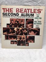 Front cover of The Beatles 'Second Album' vinyl record showing the album title, band member photos, and featured tracks titles including 'She Loves You' and 'Roll Over Beethoven'. Some wear and slight discoloration visible.