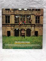 Back cover of Hot Rocks 1964-1971 vinyl record showing band members sitting on a ledge of a stone building with grass foreground.