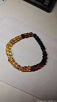 Photo of a Baltic amber bead bracelet showing gradient coloring from light yellow to dark brown beads, laid flat on paper.