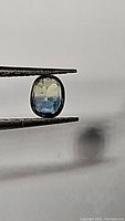 Close-up of a single bi-colored blue and yellow sapphire held by tweezers showcasing its oval cut and transparency.