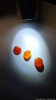 Three polished Mandarin Carnelian stones illuminated by torch light showing their orange glow and translucency.