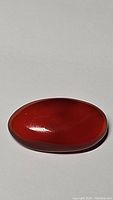 Image shows polished oval cabochon red carnelian gemstone with smooth surface and rich deep red color.