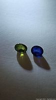 Pair of oval cabochon cut sapphire gemstones, one mint green and one royal blue, placed side by side on a white surface highlighting their clarity and colors.