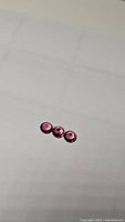 Three round pink Umbalite garnet gemstones, diamond cut, approx 5mm size each, placed on white surface.