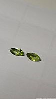 Close up photo of two marquis cut apple green peridot gemstones on white background showing color and cut.
