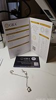 Photo of GRA certified moissanite grading report booklet alongside the heart-shaped pendant necklace on chain.