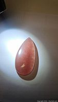 Top-down photo of the pear-shaped strawberry quartz cabochon with light reflection showing the stone's translucent pink color and internal sparkle.