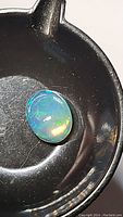 Oval cabochon Ethiopian opal on black surface showing play-of-color including blue, green, and orange hues under light.