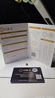 Photo showing GRA grading report and warranty certificate with loose moissanite gem on a white surface