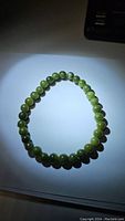 Full view of natural green jade bead bracelet with round beads strung on an elastic cord shown on a white surface under light.