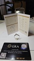 Moissanite ring in front of the GRA certificate and warranty card showing authenticity and certification details.