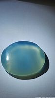 Oval ice blue chalcedony cabochon gemstone shown on white background to display color and surface quality.