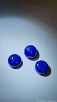 Photo showing three deep blue round cabochon Lapis Lazuli stones under direct light to highlight color and surface.