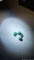 Four natural malachite oval cabochons arranged illuminated on a white surface showing their banding patterns.