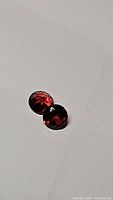 Close up photo of two round cut garnet gemstones showing the cherry red color and diamond cut facets.