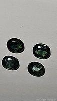 Four oval cut multicolored blue-green sapphires displayed on a light background showing color and clarity.