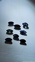 Eight natural deep blue marquise cut sapphires arranged randomly on a light background showing color and shape.