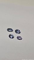Four light blue oval cut sapphires arranged on a neutral background showing their color and clarity.