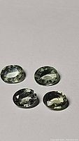 Four oval cut natural moss green sapphires on a plain background showing shape, color, and internal moss-like inclusions.