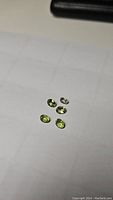 Five small oval cut peridot gemstones displayed on a white grid surface.