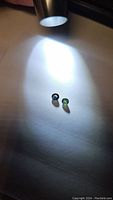 Photo of two small round sapphires on a white surface under focused light, showing green and green-blue colors
