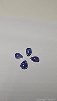 Four pear-shaped cabochon tanzanite gemstones on white background, showing polished smooth surfaces and purple-blue color.