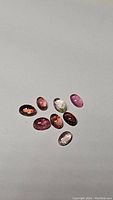 Photo showing eight natural oval cabochon tourmaline gemstones in various colors arranged on a light background.