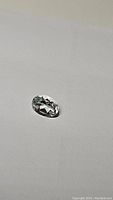 Close-up photo of an oval cut white topaz gemstone placed on a white background, showcasing its faceted polished surface and clarity.