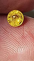Close-up photo of a small round cut bright lemon yellow sapphire gemstone on a fingertip, showing facets and clarity.
