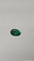 Photo of the oval cut emerald on a plain surface showing the green color and internal inclusions.