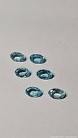 Five oval cut Paraiba blue colored apatite gemstones against a plain background showing clarity and cut.