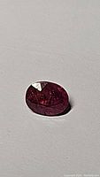 Close-up image of oval cut natural pink sapphire gemstone on a gray background showing color and inclusions.