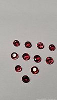 Top down view of 11 round cut rubies with deep hot pink-red-orange tint on white background, showing clarity and color uniformity